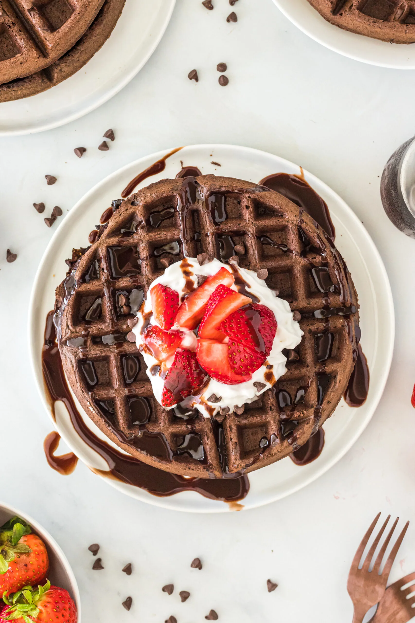 top view looking down at chocolate waffle topped with whipped cream, strawberries and chocolate syrup