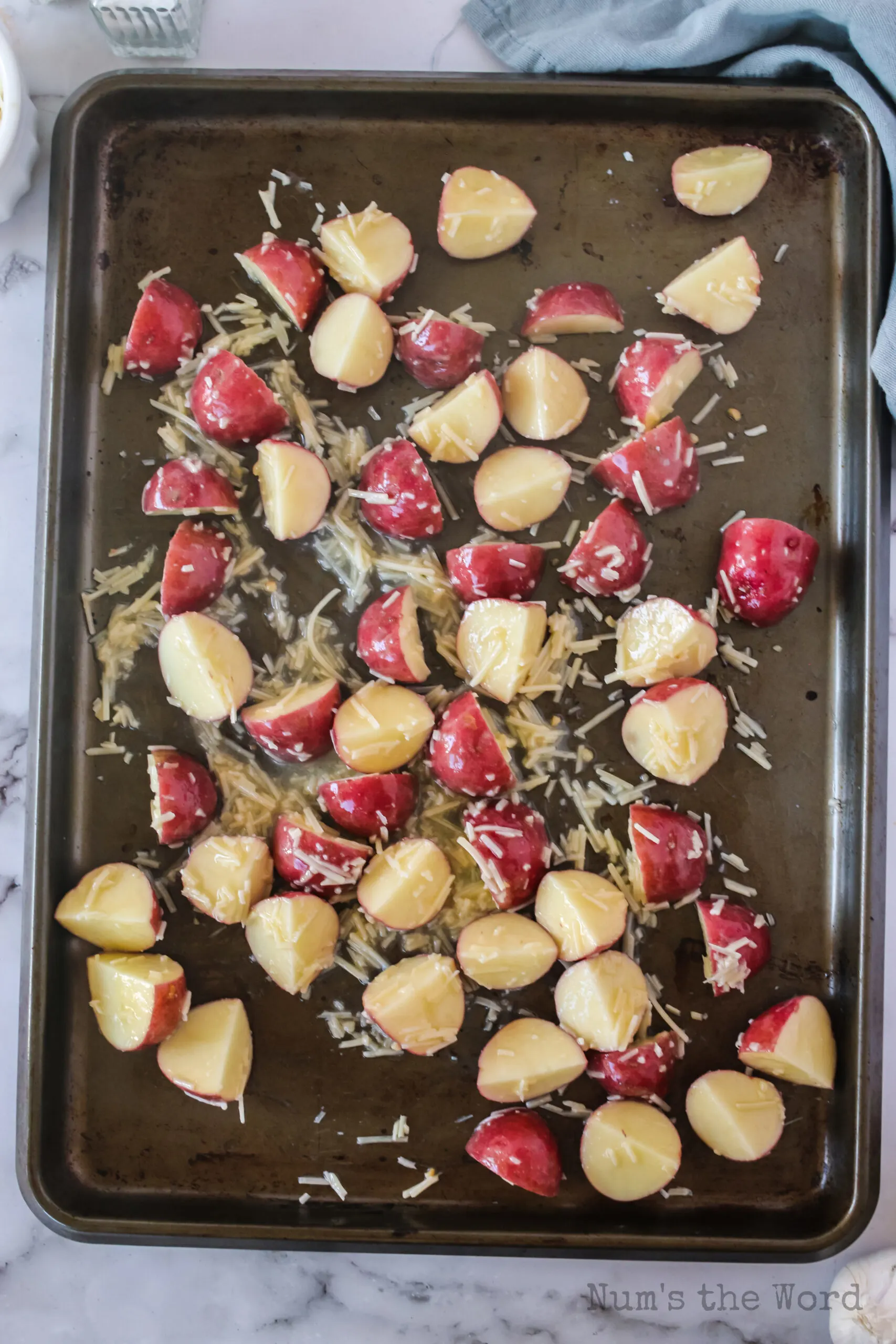 Potatoes mixed with butter and parmesan spread out on a cookie sheet