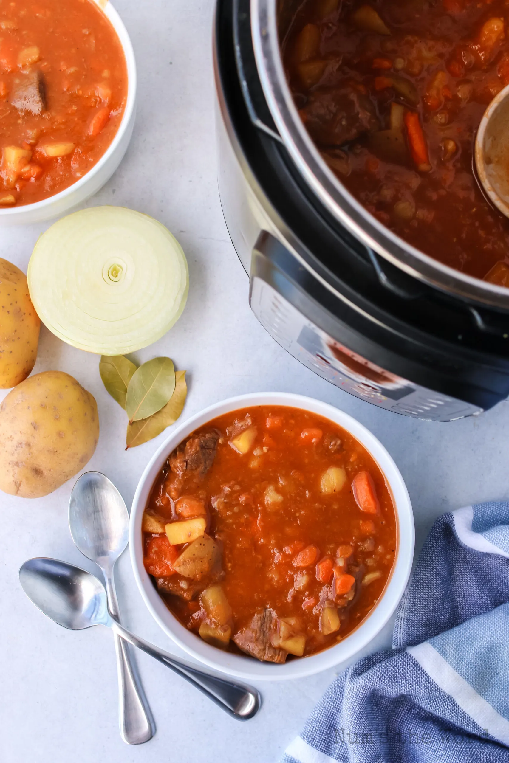 zoomed out image of beef stew in two bowls and in the instant pot with ingredients all around