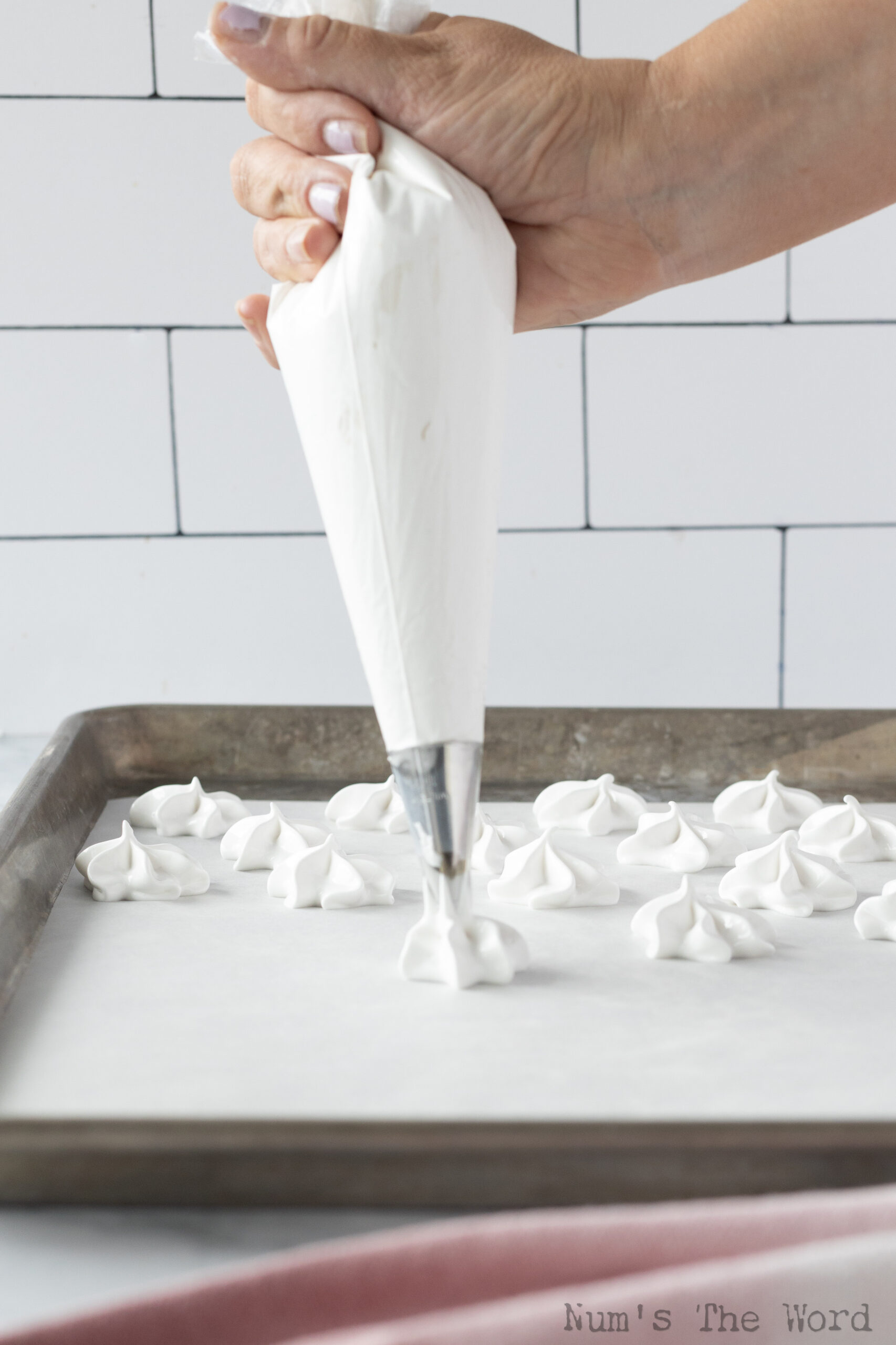 piping bag with a star tip filled with meringue batter piping out stars on a line cookie sheet