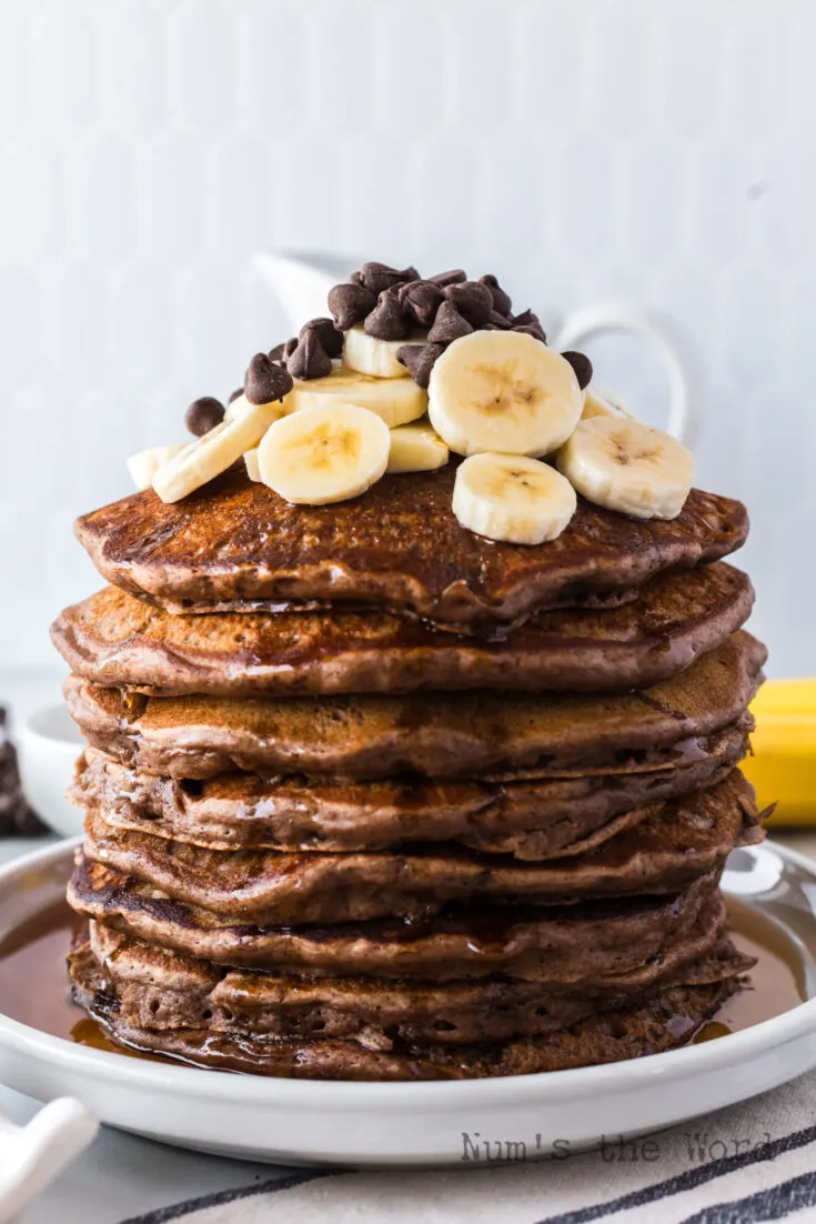 stack of pancakes topped with butter, maple syrup, fresh bananas and chocolate chips