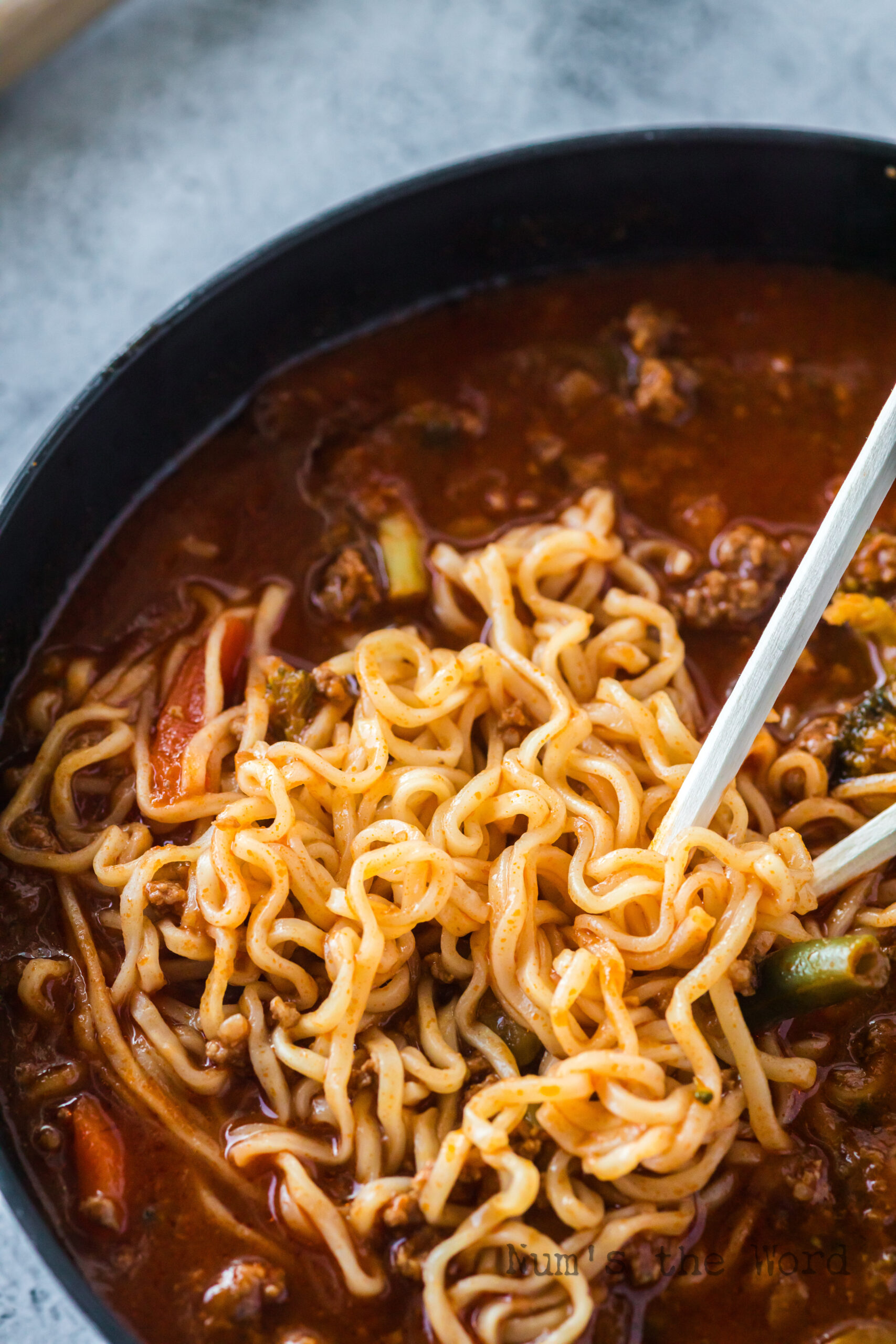 zoomed in image of soup in bowl with chop sticks pulling noodles