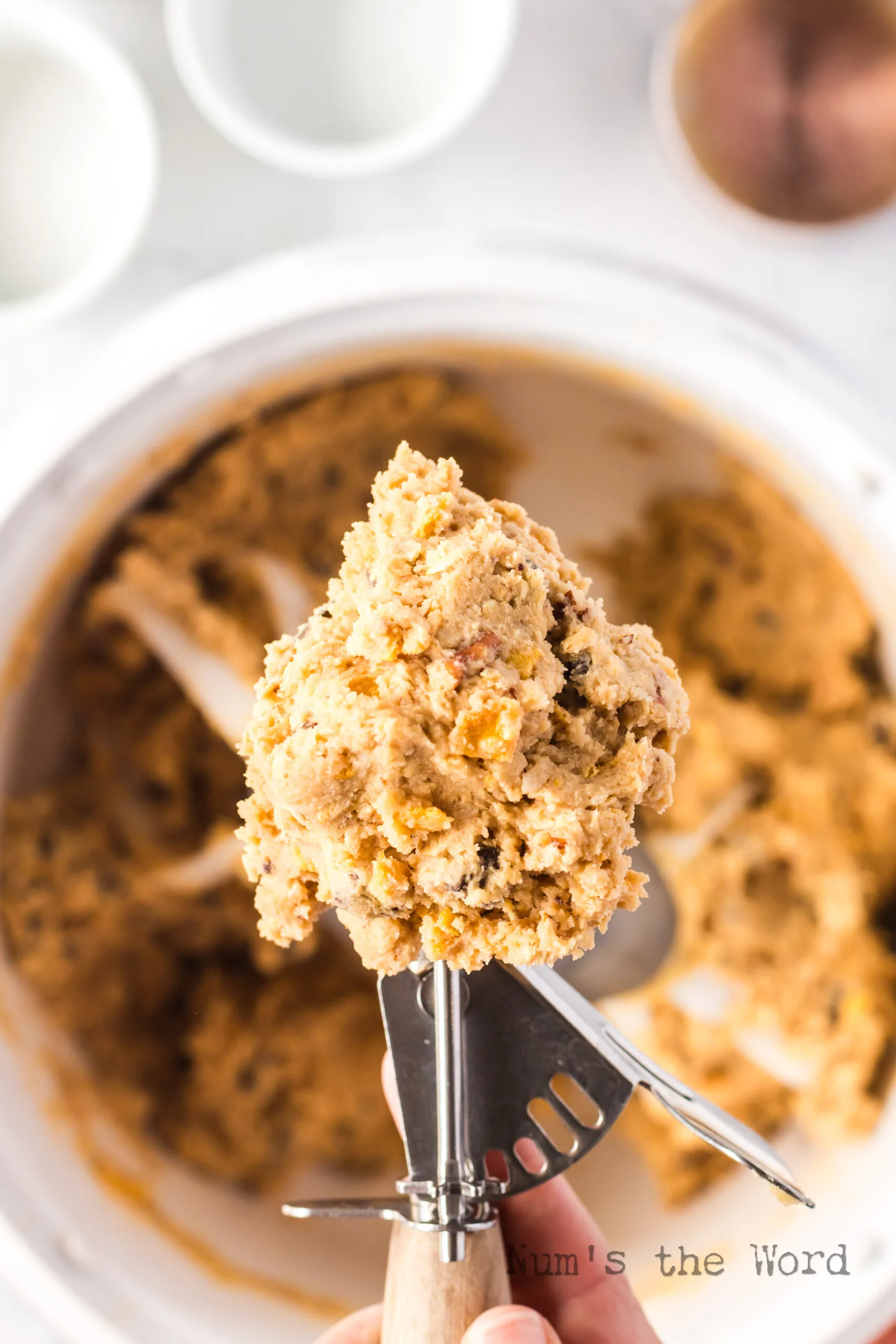 cookie scoop full of dough above bowl full of cookie dough