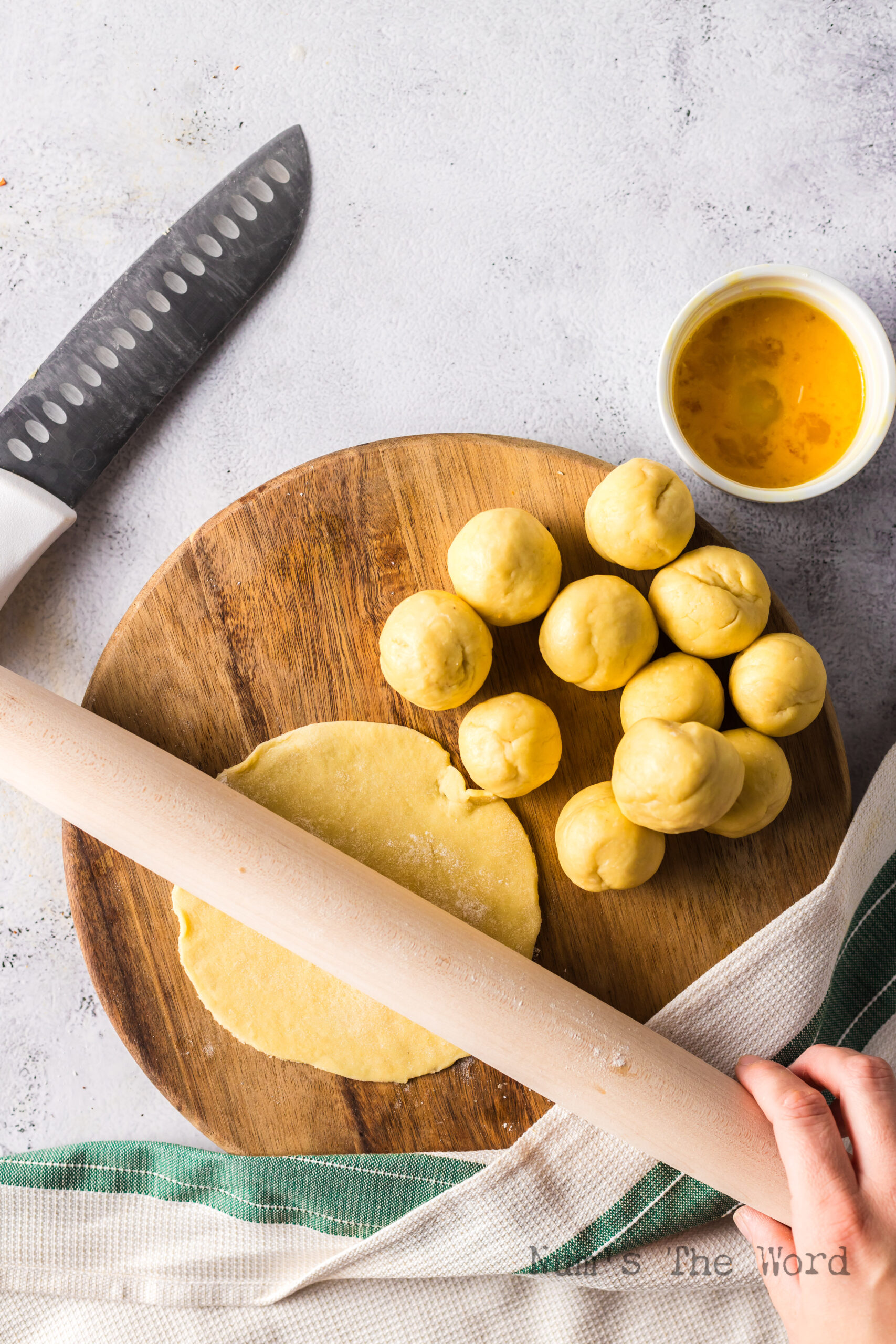 12 dough balls laid out on cutting board with one being rolled into a circle.