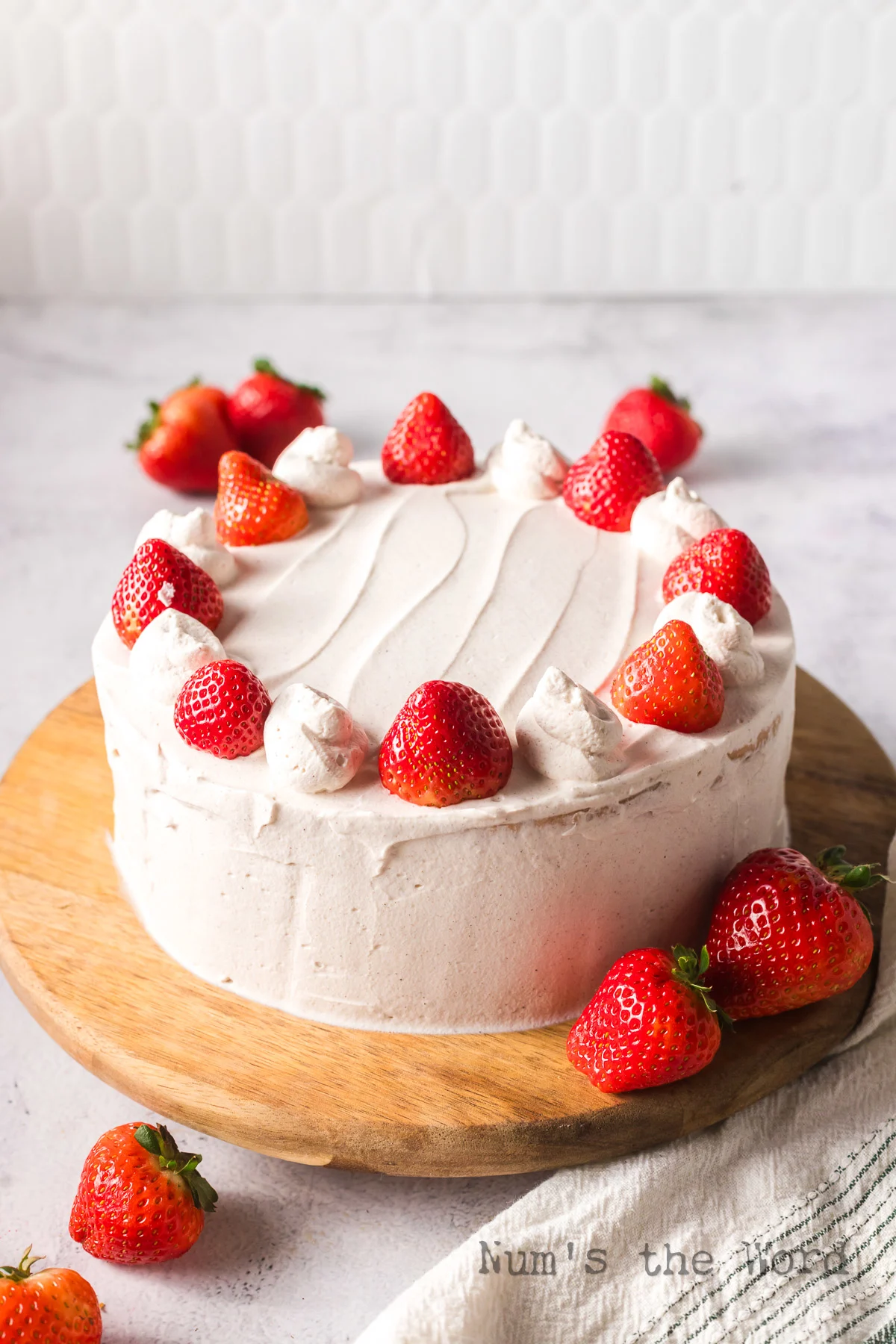 side angled view of frosted cake with extra piped frosting and strawberries