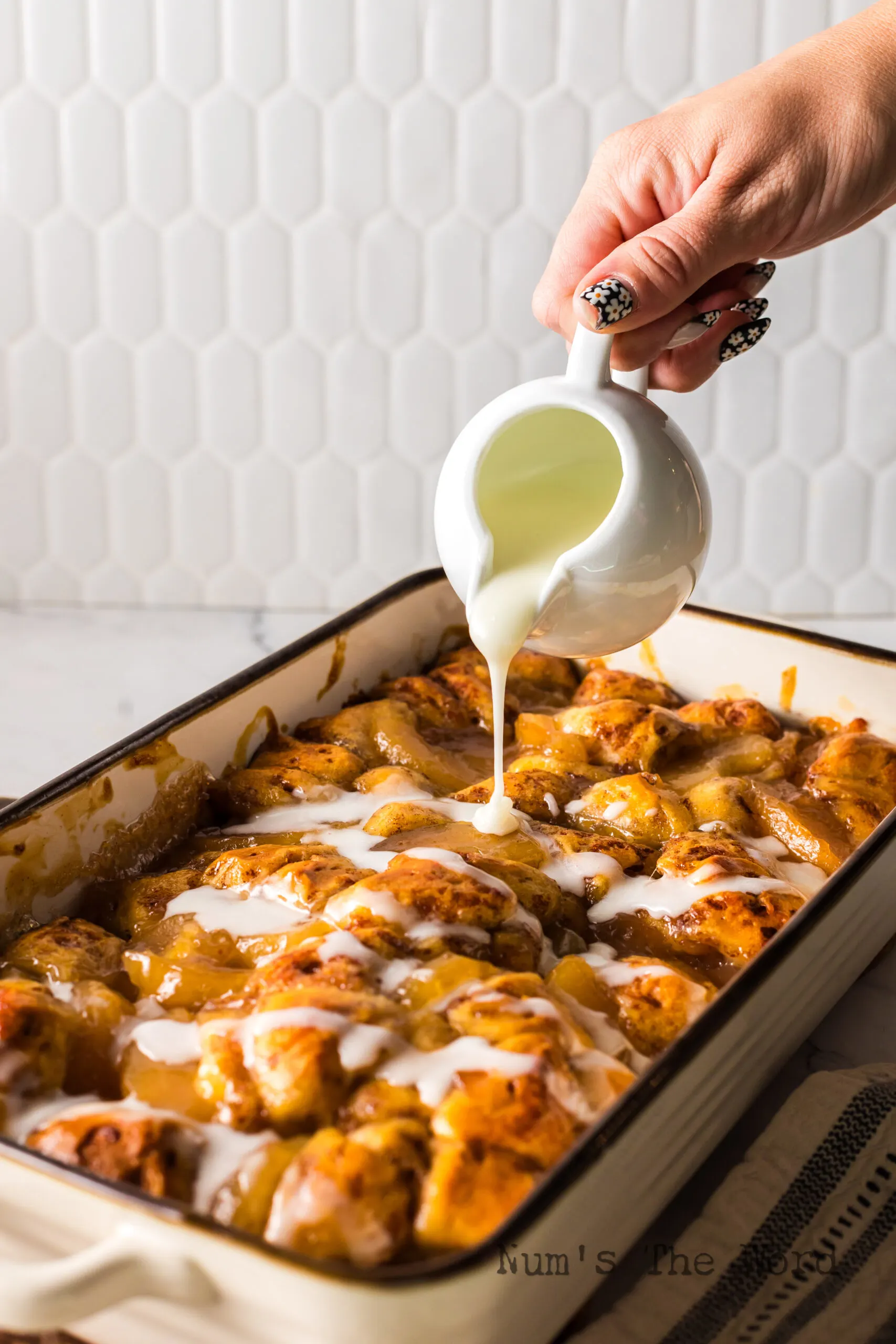 Icing being drizzled on top of cinnamon rolls