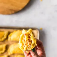Hand holding an empanada up with filling showing.