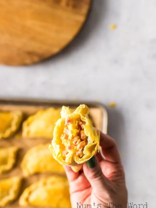 Hand holding an empanada up with filling showing.