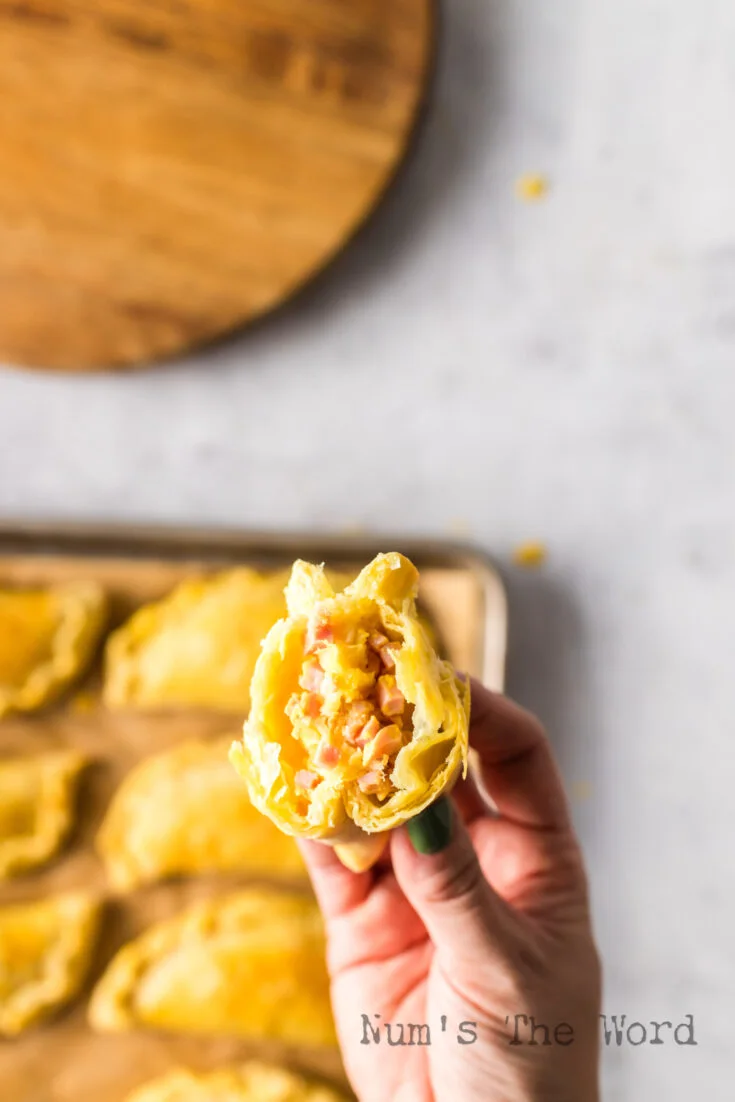 Hand holding an empanada up with filling showing.