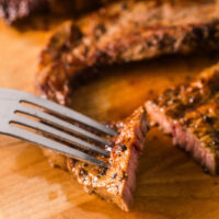 fork and knife cutting a piece of steak on a cutting board.