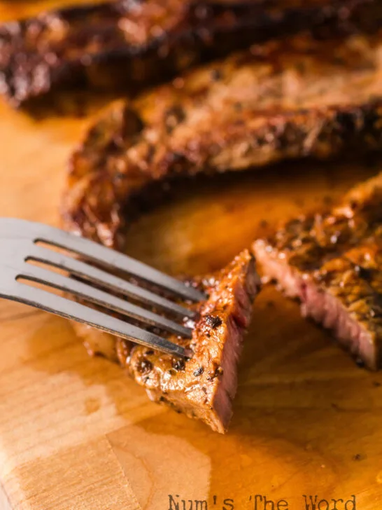 fork and knife cutting a piece of steak on a cutting board.