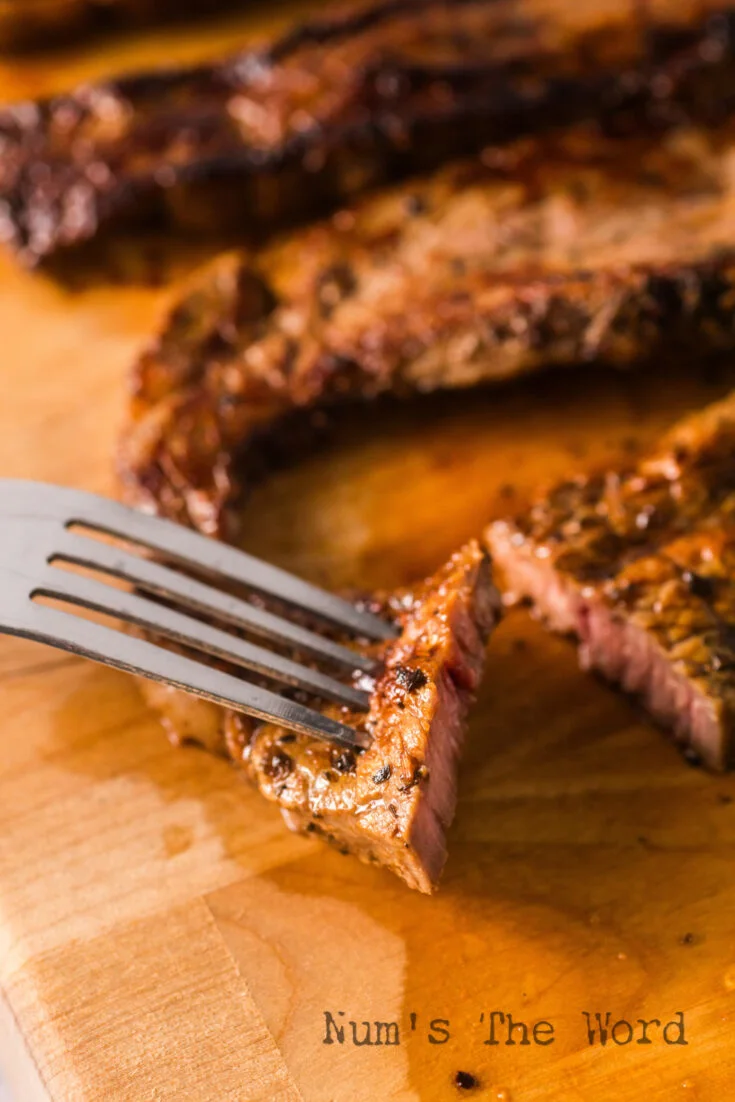 fork and knife cutting a piece of steak on a cutting board.
