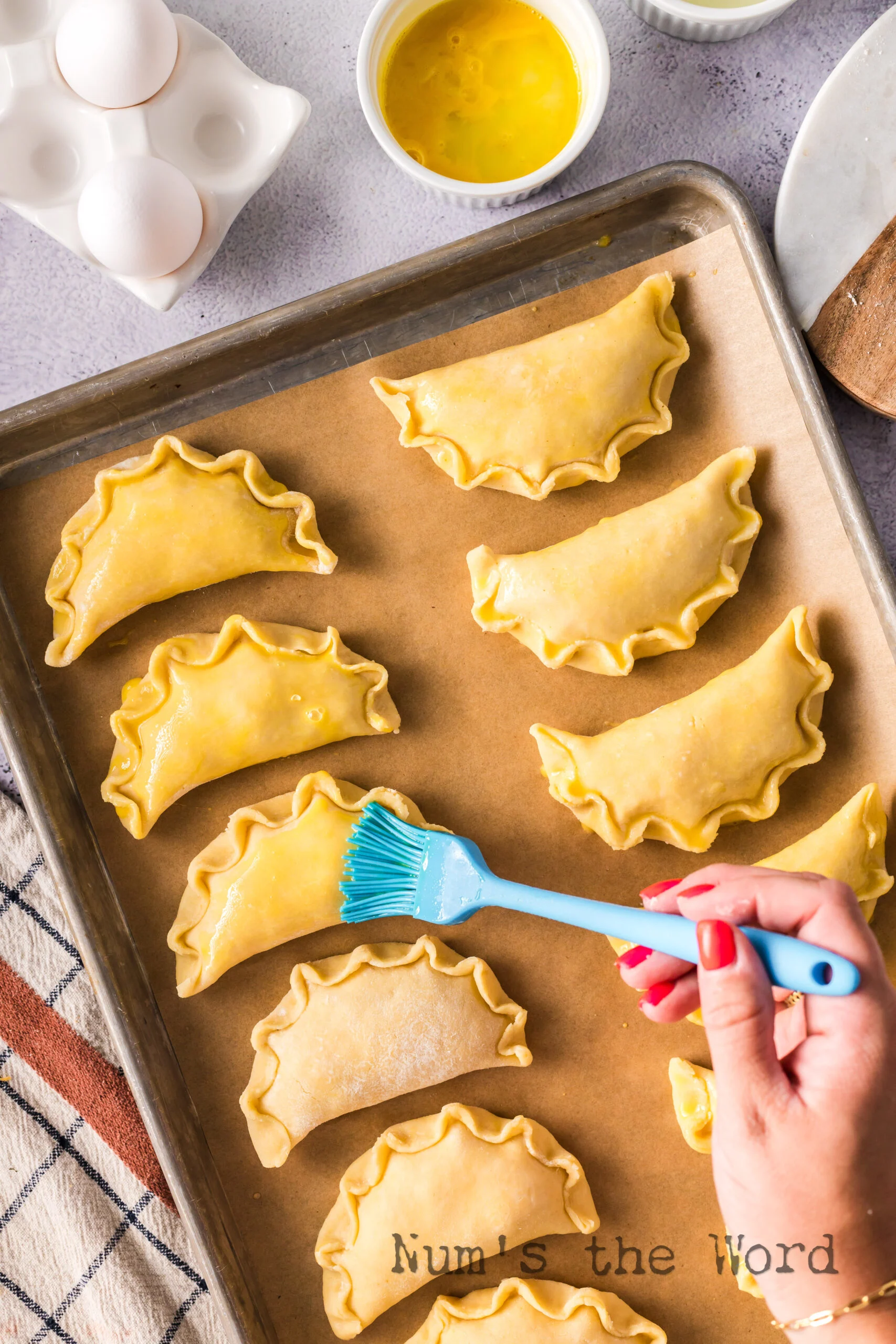 brushing unbaked empanadas on a baking sheet with egg wash.