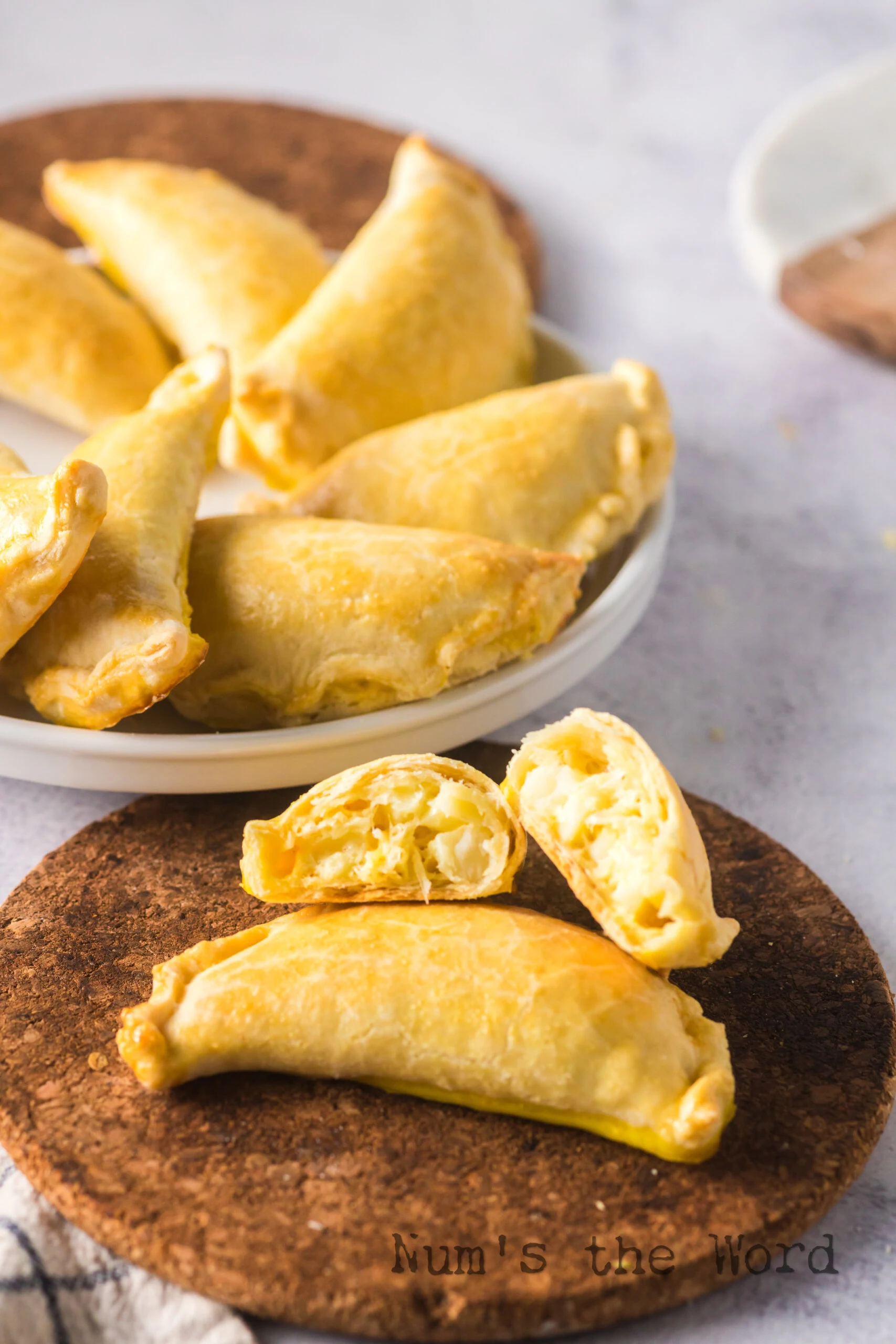a plate full of empanadas in the background with two in the foreground. One is cut open to show filling.
