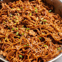 cooked chicken and noodles in pan with green onions.