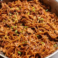 cooked chicken and noodles in pan with green onions.