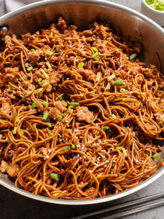 cooked chicken and noodles in pan with green onions.