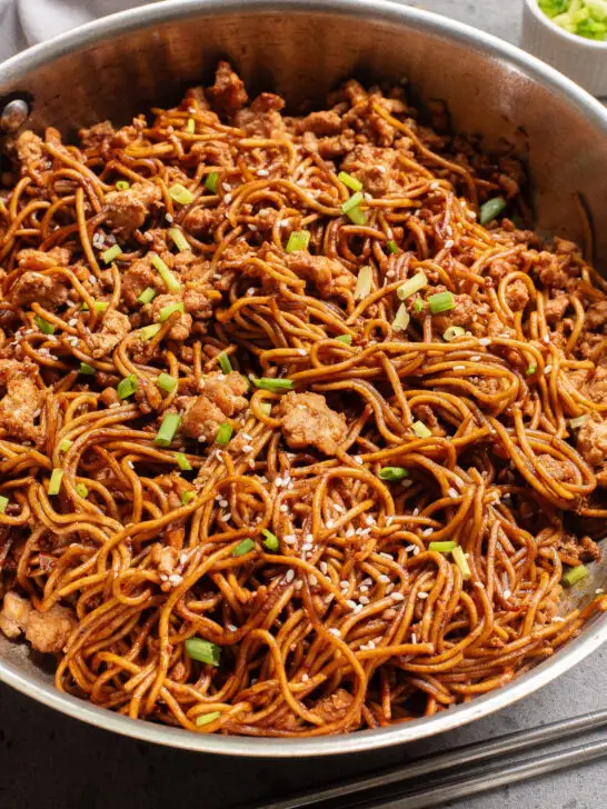 cooked chicken and noodles in pan with green onions.