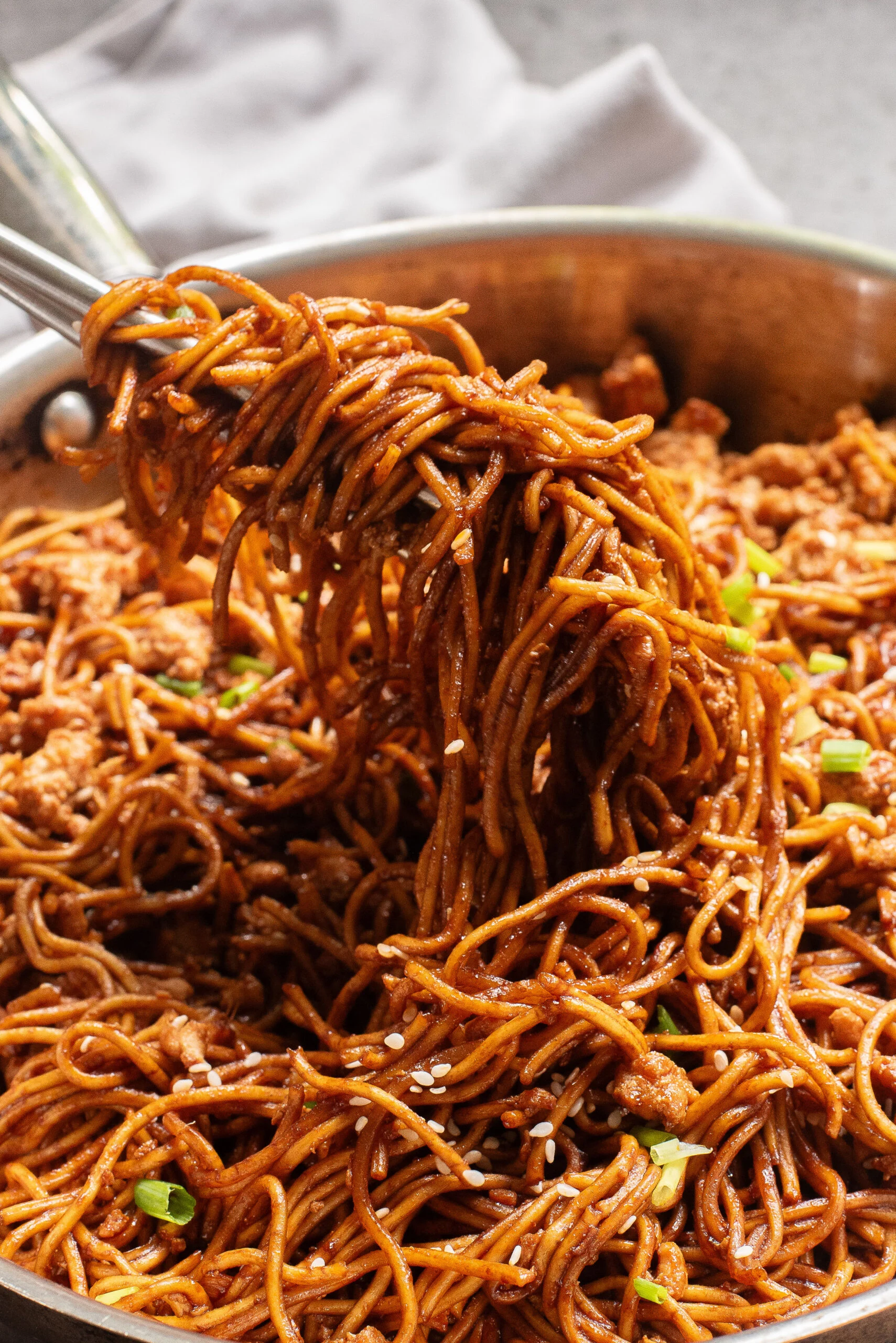 cooked noodles and chicken being scooped out of pan with chop sticks.