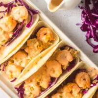 5 prepared tacos with sauce drizzled over the top.