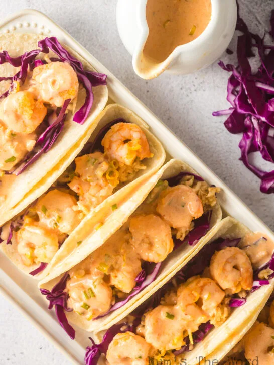 5 prepared tacos with sauce drizzled over the top.