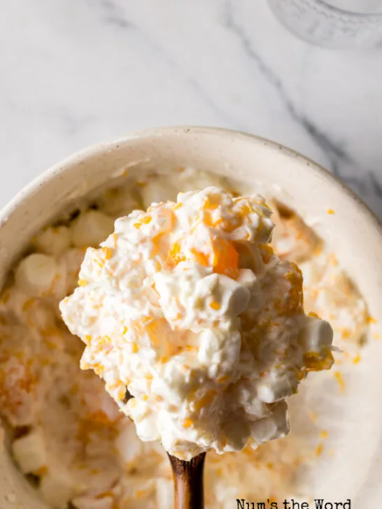 top view looking down at fruit salad with a wooden spoon scooping some out of the bowl.