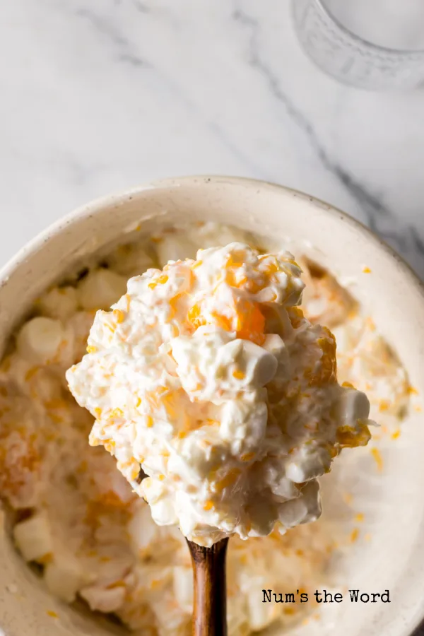 top view looking down at fruit salad with a wooden spoon scooping some out of the bowl.