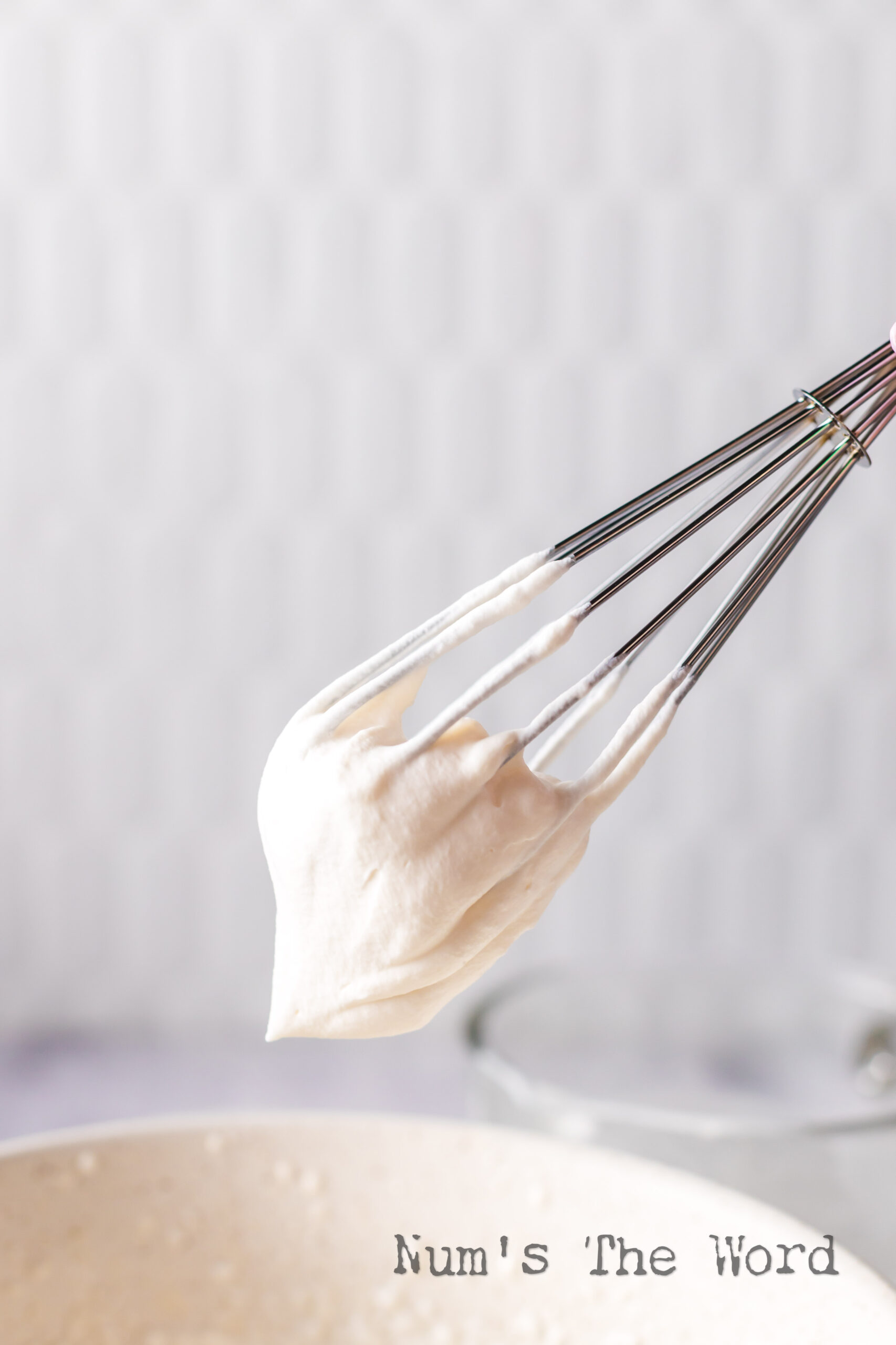 whisk being held above the bowl showing a stiff peak