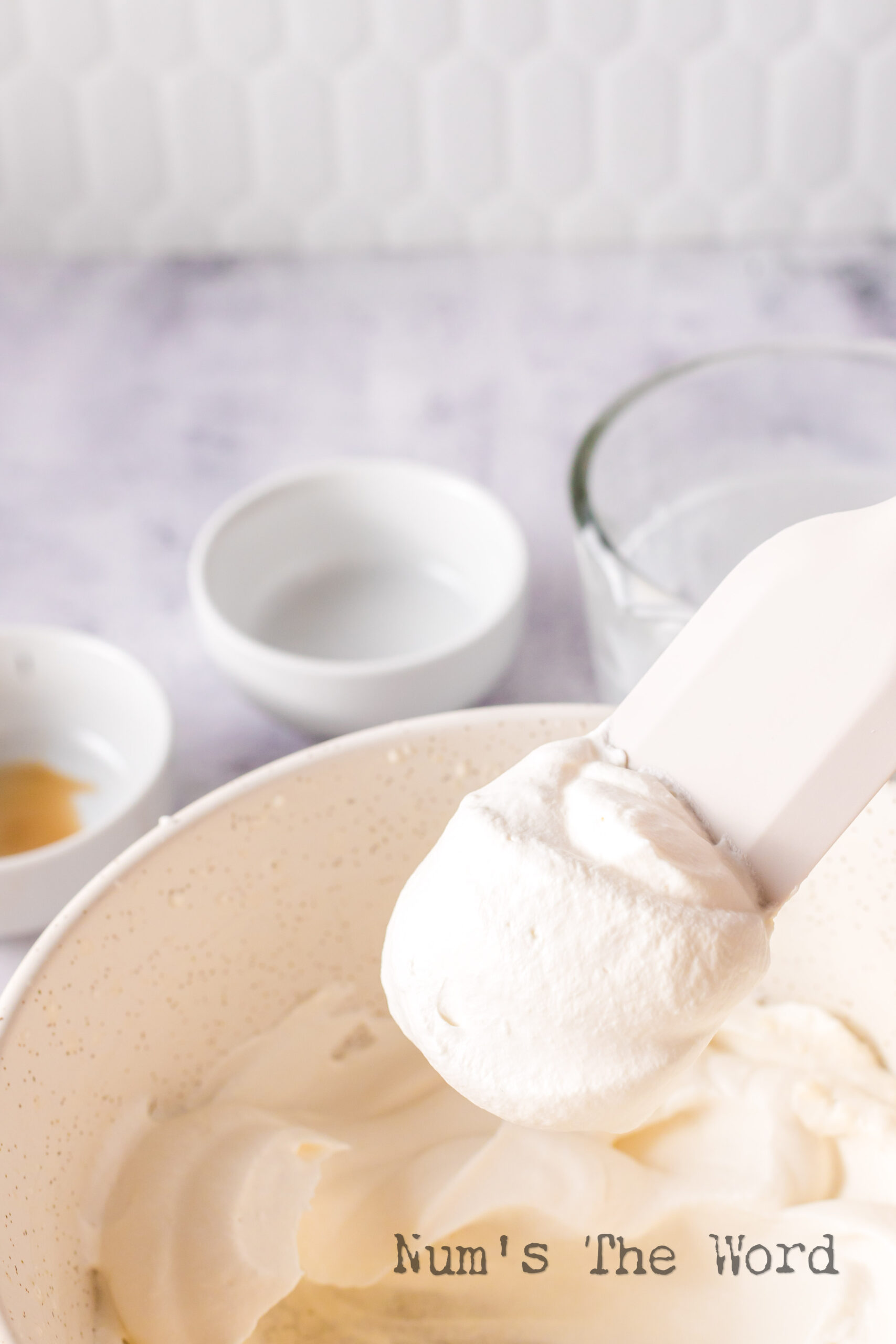 rubber spatula scooping a portion of whipped cream out of bowl.