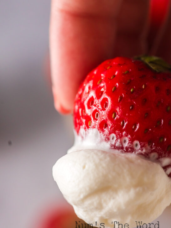 Hand holding a strawberry covered in whipped cream
