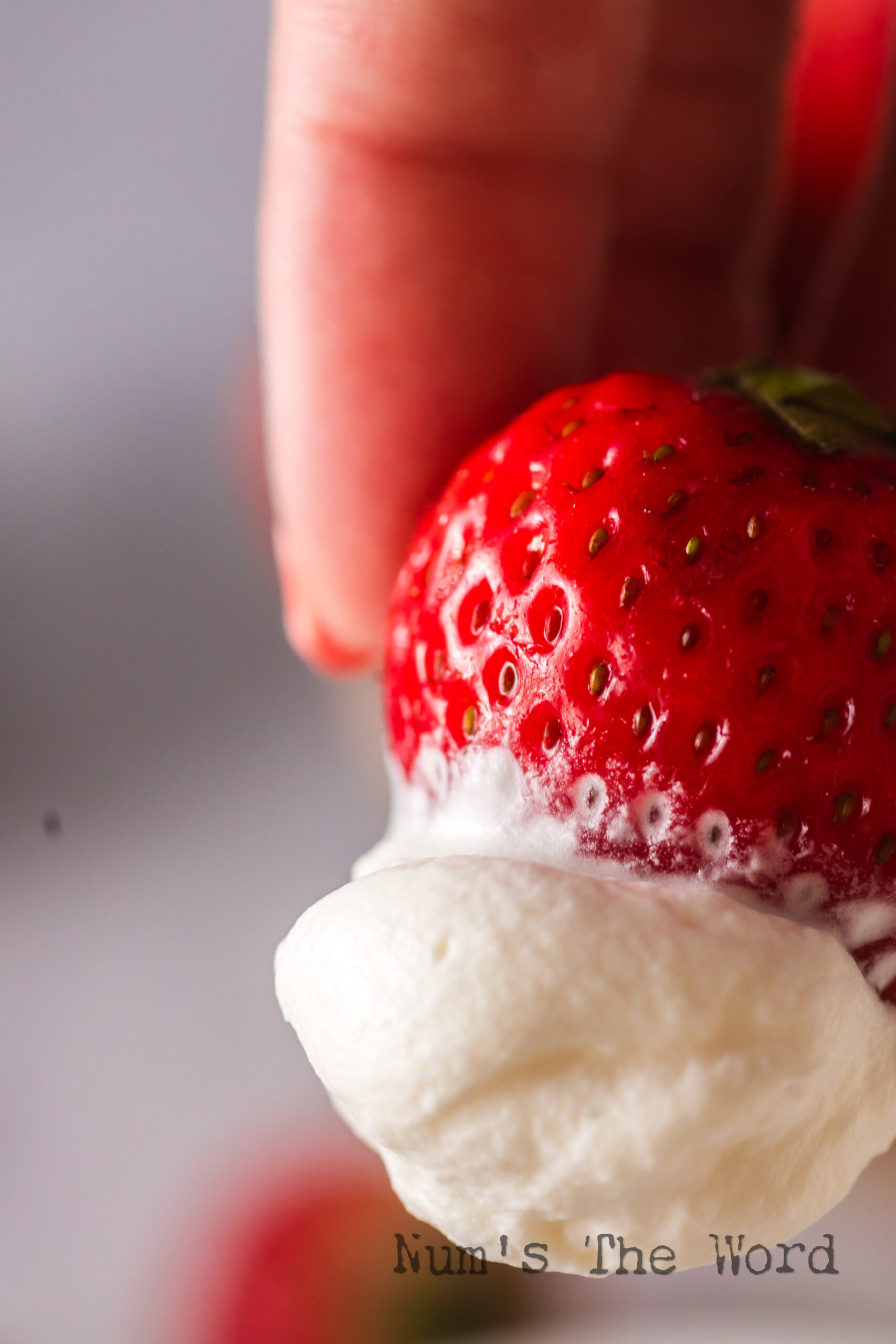 Hand holding a strawberry covered in whipped cream